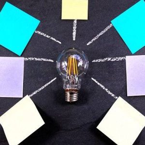 light bulb on a dark grey background surrounded by 7 white lines each pointing to a different coloured post it note